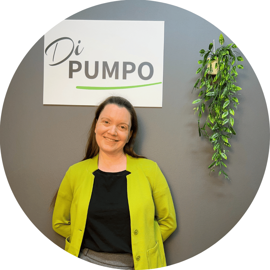 Frau mit langen Haaren in einem grünen Blazer vor einem Schild mit "Di PUMPO".