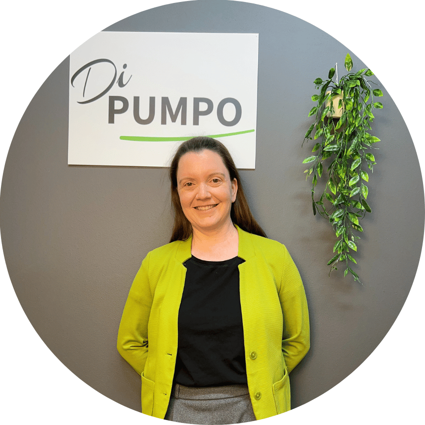 Frau mit grüner Jacke lächelt vor einer Wand mit dem Schriftzug „Di PUMPO“.